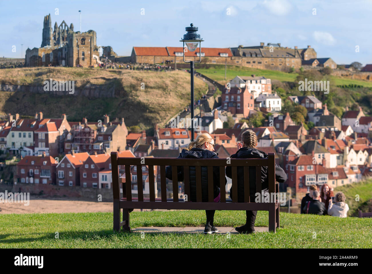 Due femmine seduto su una panca in legno che si affaccia su persone utilizzando la 199 passi a Whitby Abbey e la chiesa di Santa Maria Foto Stock