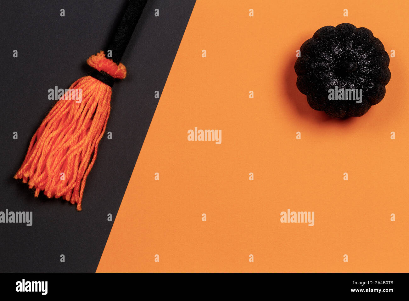 Sfondo di Halloween. Decorativo lucido nero zucca su sfondo arancione e la scopa della strega su sfondo nero. Vista superiore Foto Stock
