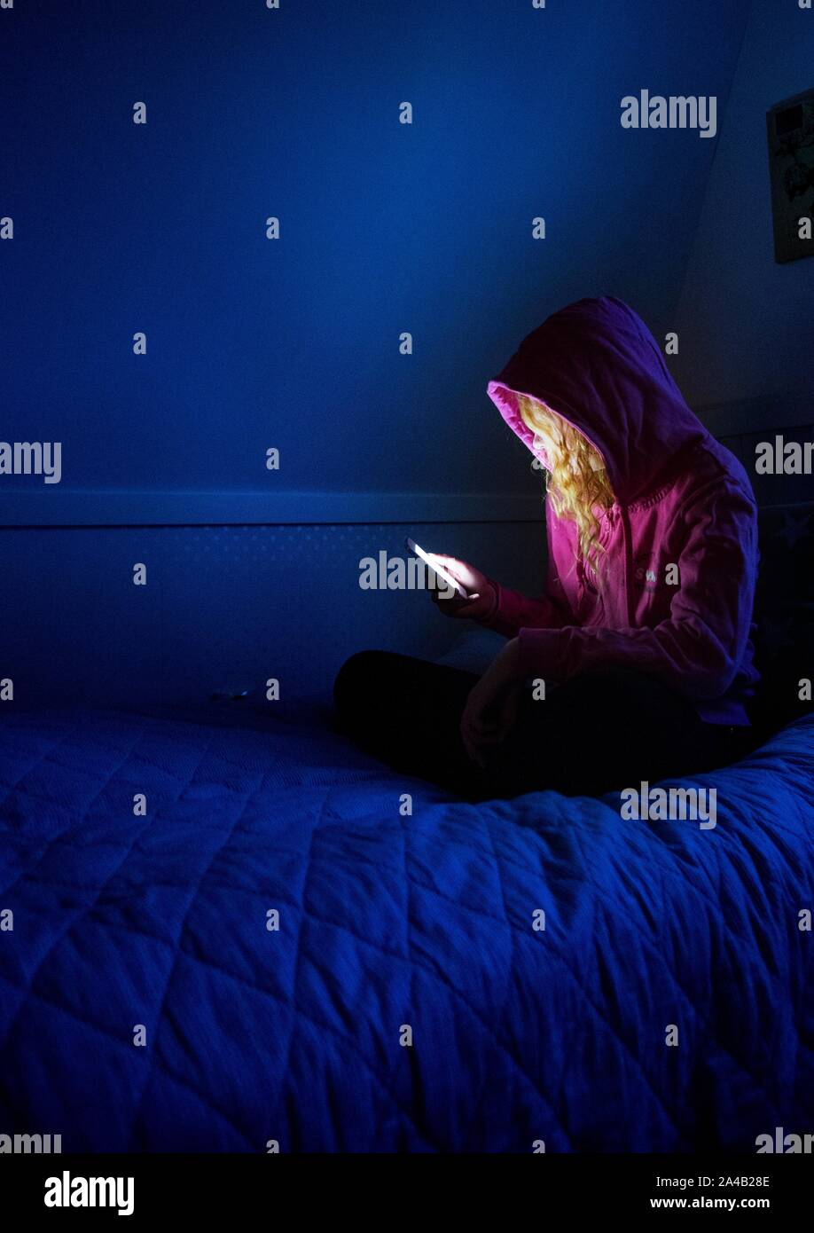 Una ragazza seduta con il telefono cellulare in camera sua.Photo Jeppe Gustafsson Foto Stock