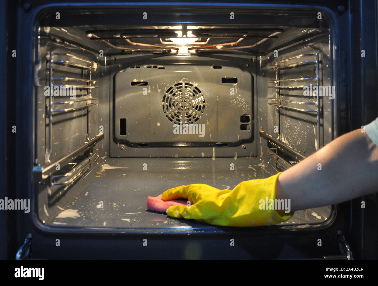 La pulizia del forno in cucina. mano in un giallo guanto per uso domestico fuori fuoco sullo sfondo del forno. Foto Stock