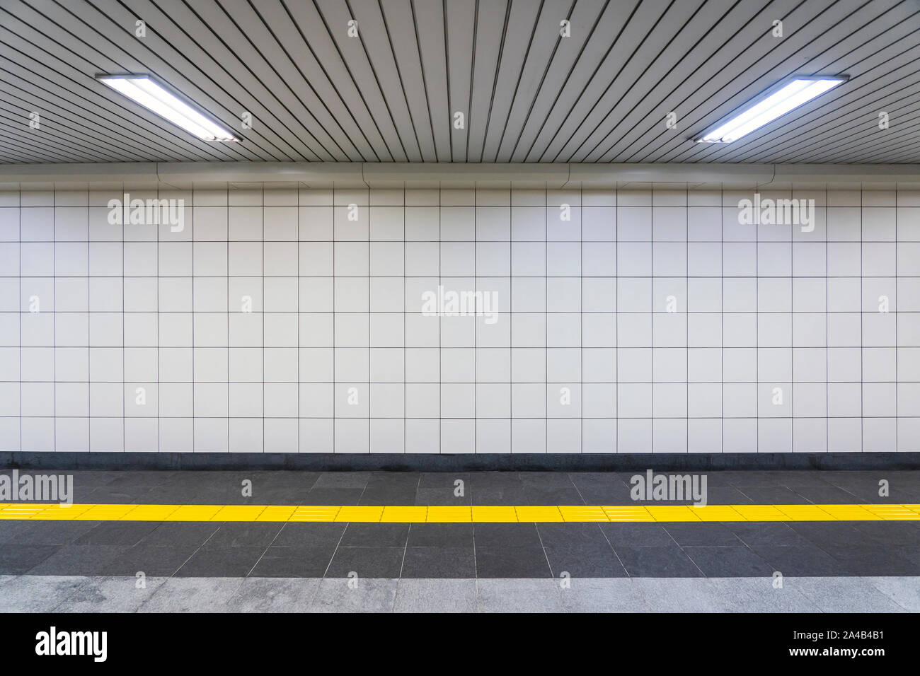 Vista ingrandita di un pubblico regolare di corridoio. Nessuno è nel tunnel con quadrato bianco piastrelle, giallo con pavimentazioni tattili e soffitto bianco luci. Foto Stock