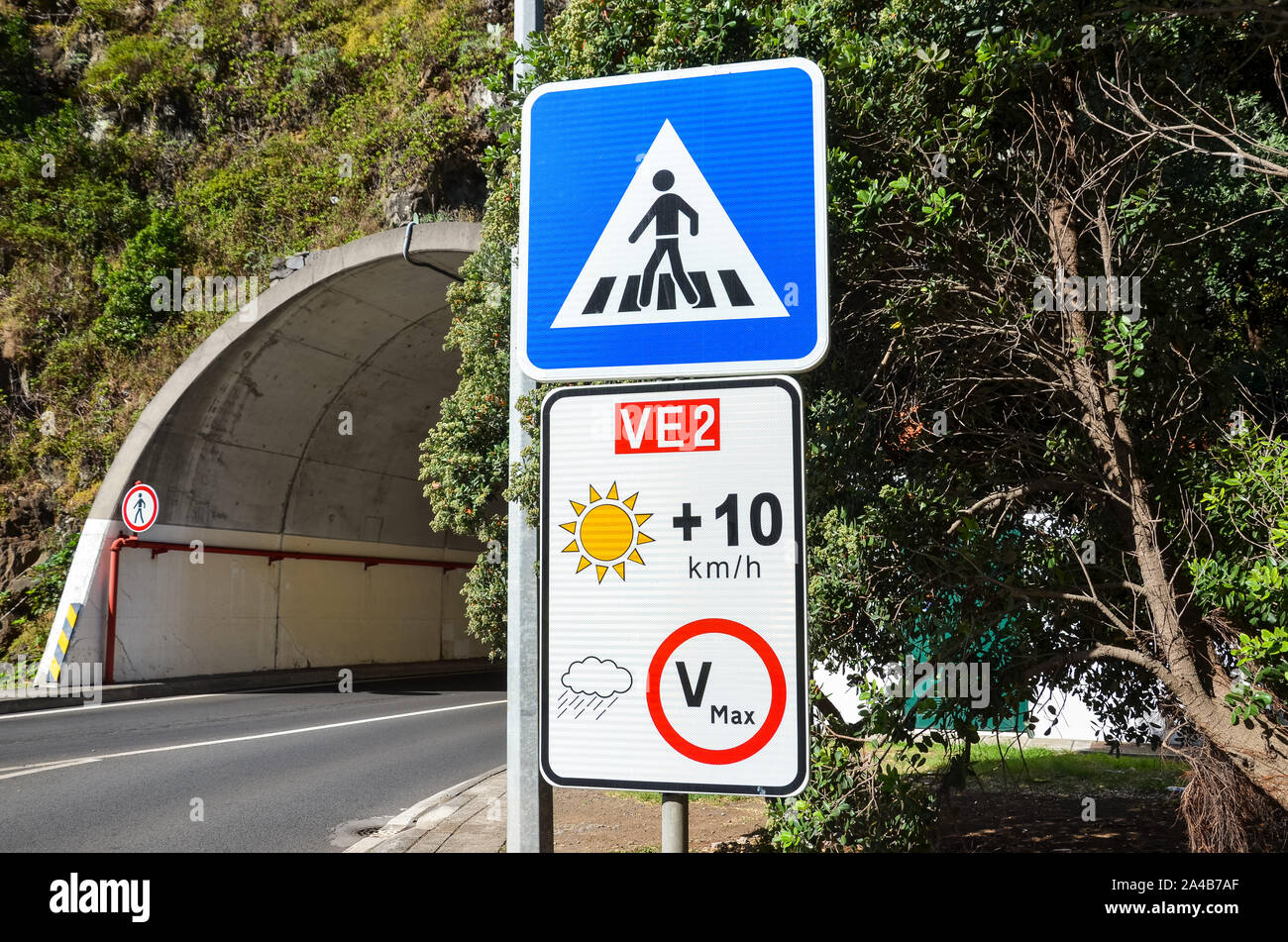 I cartelli stradali in Madeira, Portogallo. Blue zebra crossing segno. Bianco segnale di limite di velocità. La limitazione di velocità è dipendente sul meteo, in caso di cielo chiaro il limite è più 10 kmh rispetto a quanto indicato sul cartello. Foto Stock