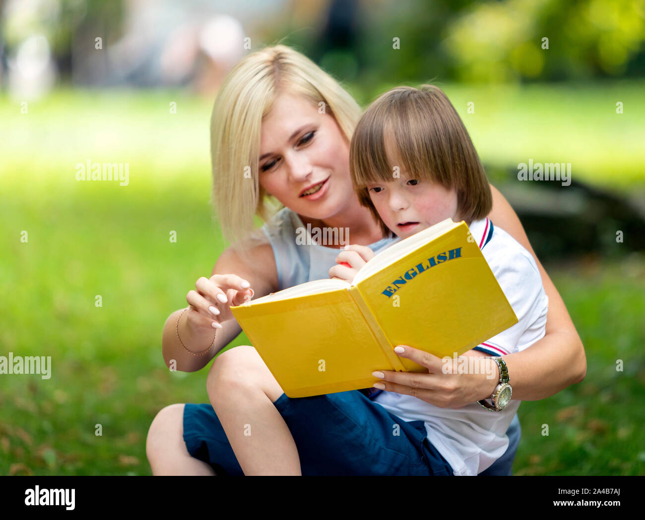 Contestato boy divertito da un libro di sua madre gli mostra su un parco Prato Foto Stock