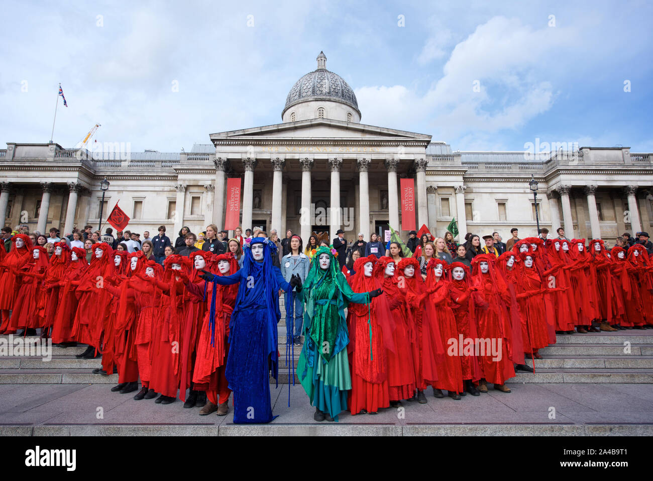 Rosso vigili del ribelle presso la Galleria Nazionale mentre i sacerdoti e i vescovi hanno preso a turno per leggere formano il libro delle Rivelazioni. Estinzione della ribellione protesta ha continuato a Londra dal 7 ottobre. Lo scopo della partecipazione di massa in non-violenta azione diretta e di disobbedienza civile è stato quello di richiamare l attenzione sulla crisi del clima e la perdita di biodiversità. Estinzione della ribellione richieste sono che i governi dire al pubblico la verità circa la reale portata della crisi, agire adesso per ridurre le emissioni di CO2 e configurare gruppi di cittadini per sorvegliare le modifiche della politica. Essi esigono inoltre che siano presi provvedimenti per far cessare l' Foto Stock