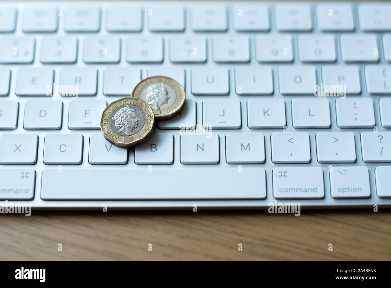 Sterlina britannica monete sulla parte superiore di una tastiera Mac prevista su di un tavolo di legno Foto Stock