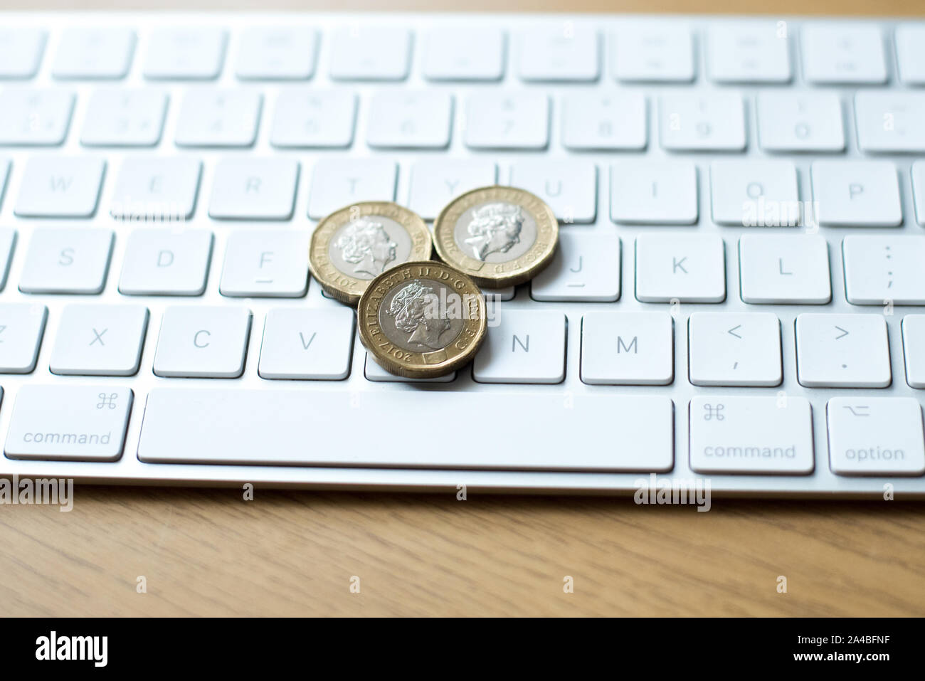 Sterlina britannica monete sulla parte superiore di una tastiera Mac prevista su di un tavolo di legno Foto Stock