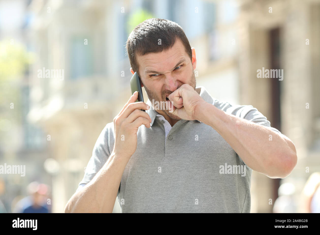 L'uomo arrabbiato parlando al telefono mobile avendo problemi in piedi in strada Foto Stock