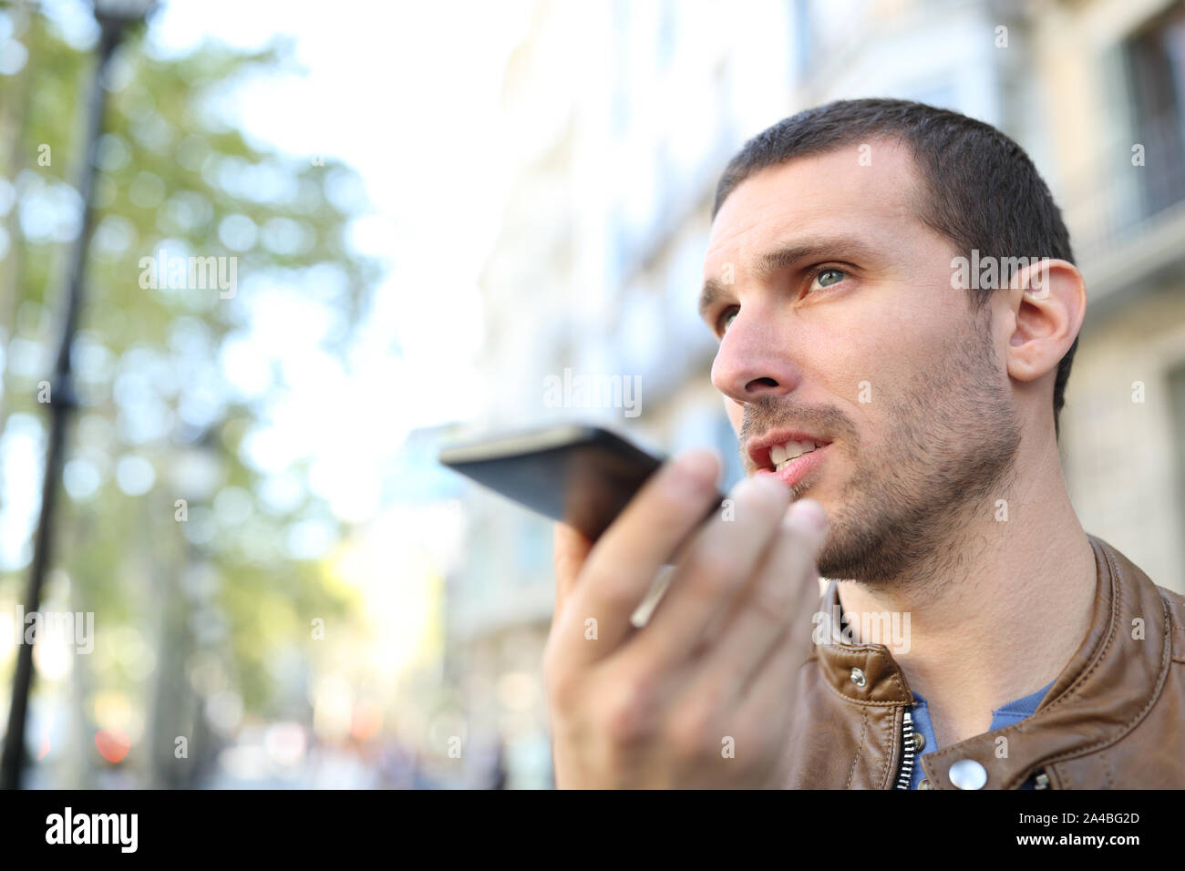 Uomo adulto usando il riconoscimento vocale sul telefono cellulare per inviare un messaggio registrato in strada Foto Stock