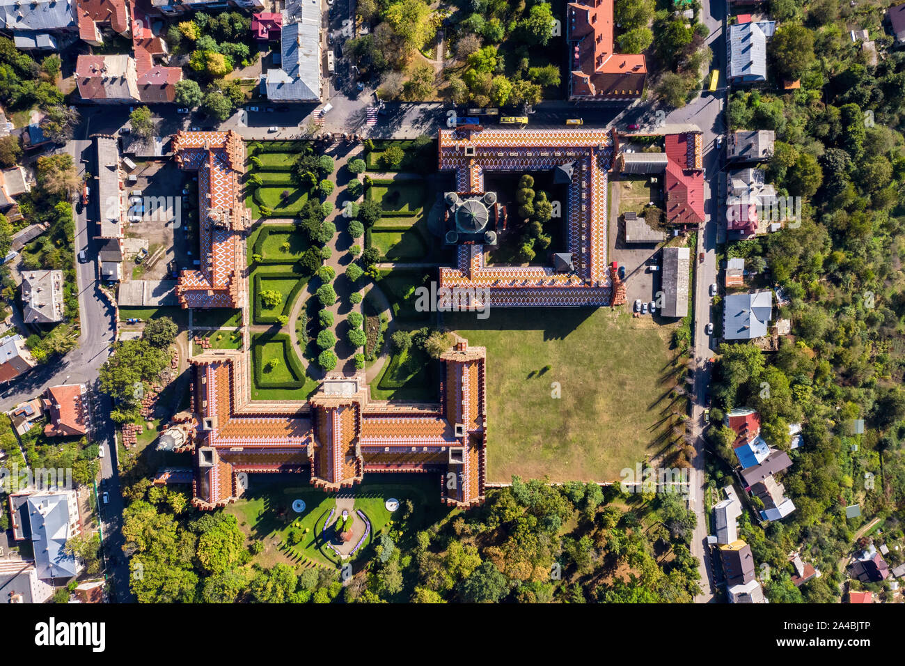 Incredibile di vecchi edifici dell'Università di Chernivtsi con torri e cupole tra alberi verdi e case in Ucraina. Sole splende su di essi. Vista superiore a Foto Stock
