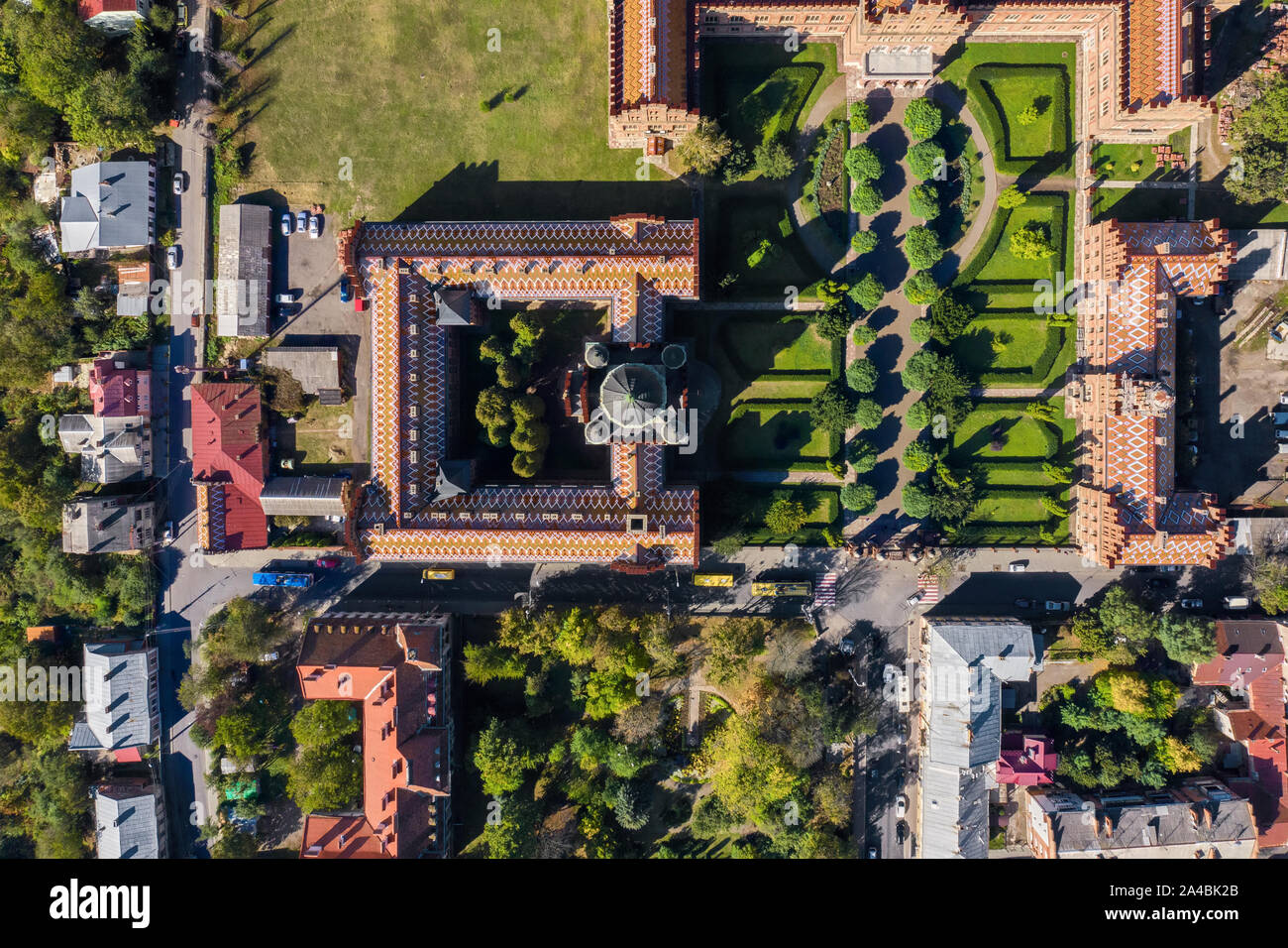 Storico di edifici dell'Università di Chernivtsi con torri e cupole tra alberi verdi e case in Ucraina. Sole splende su di essi. Top vie Foto Stock