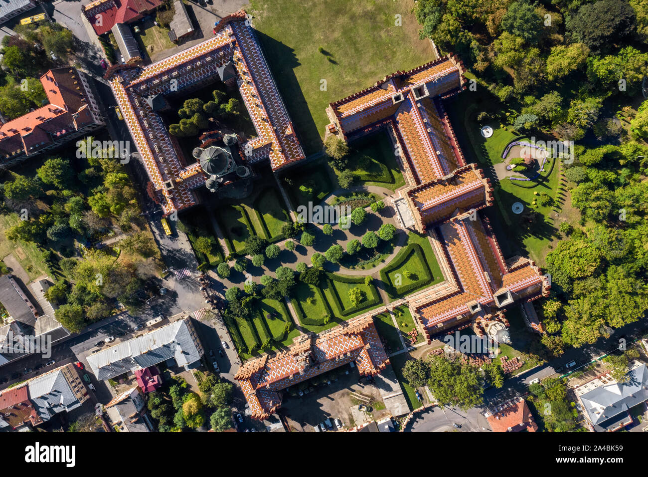 Gli edifici di vecchia costruzione dell'Università di Chernivtsi con torri e cupole tra alberi verdi e case in Ucraina. Sole splende su di essi. Vista superiore antenna pa Foto Stock
