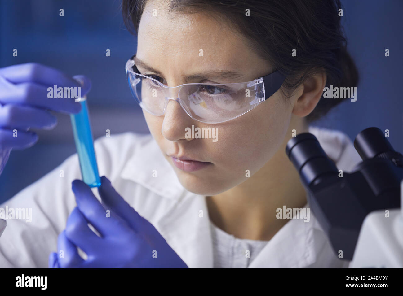 Ravvicinata di una giovane e bella donna che guarda la provetta con liquido colorato mentre si lavora sulla ricerca medica in laboratorio, spazio di copia Foto Stock