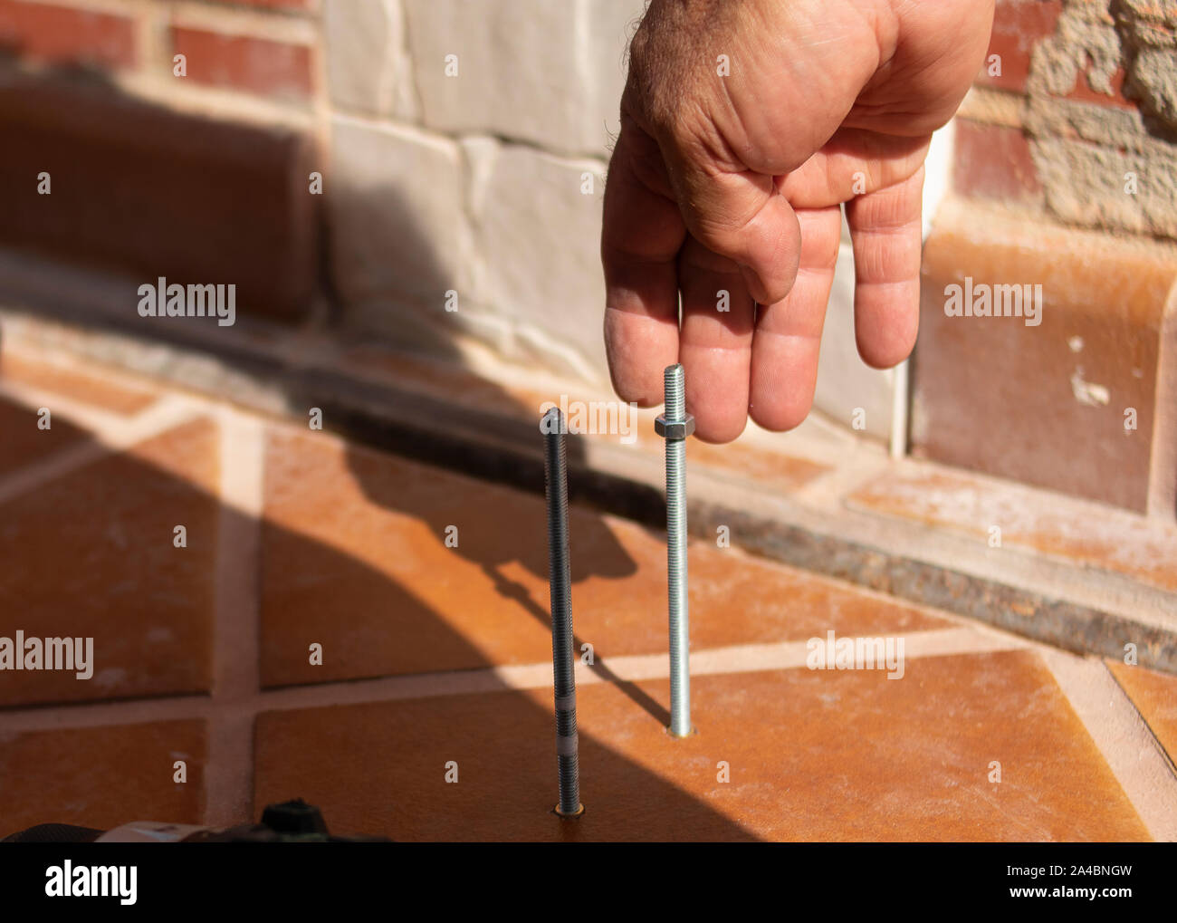 Una mano d'uomo riccioli di un dado su un asta filettata in una giornata di sole e con gli altri strumenti in un lavoro FAI DA TE Foto Stock