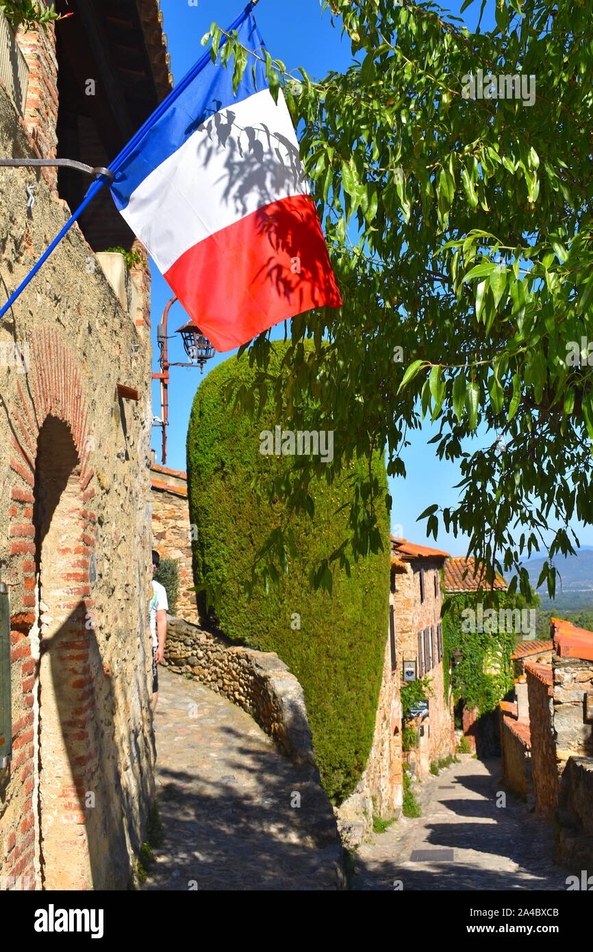 Bandiera francese che gravano su di una strada di ciottoli, piena di verde e di edifici medievali. Vicolo iconico in un affascinante unione città vecchia. Foto Stock