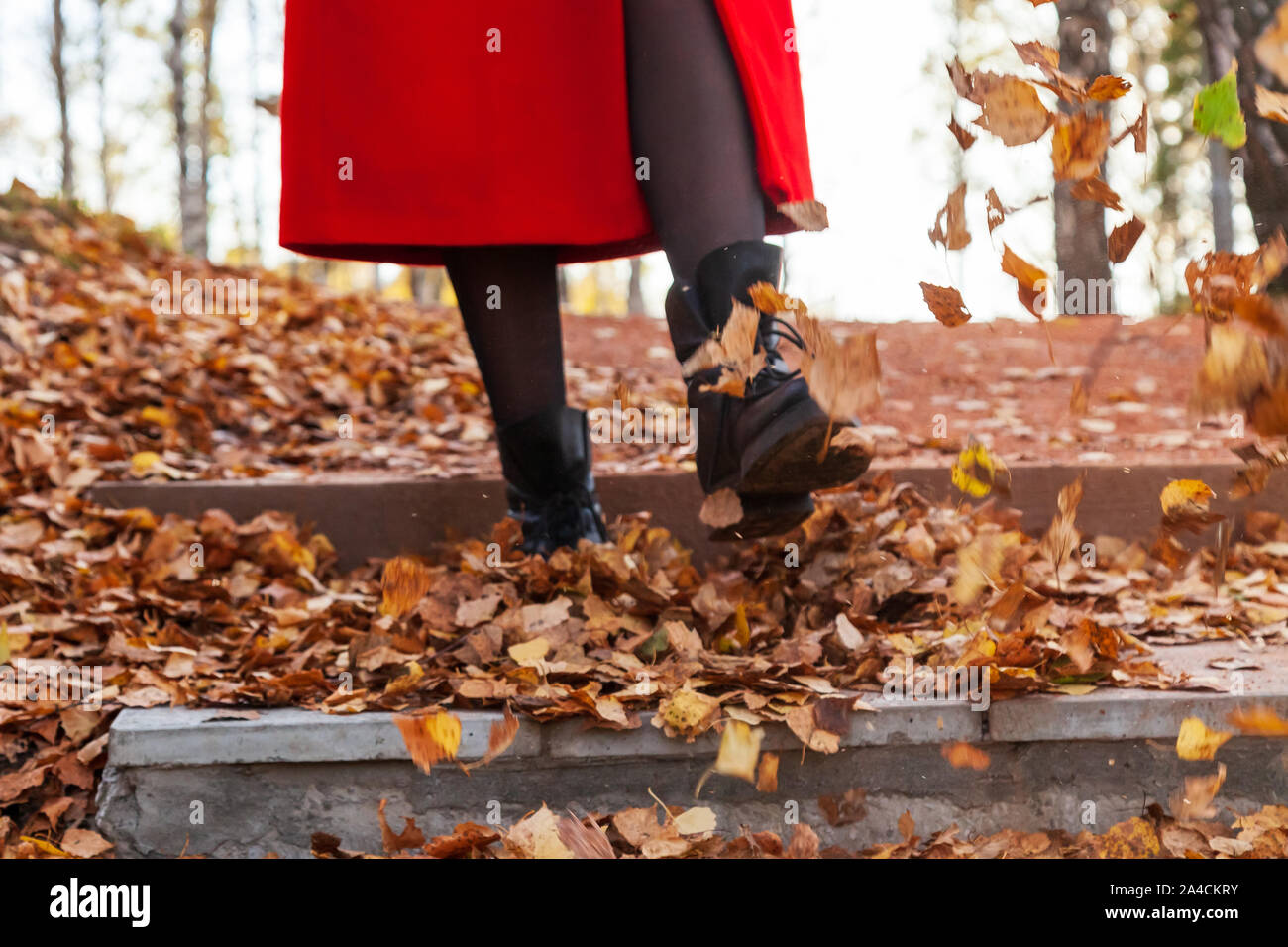 Una ragazza in stivali neri e un cappotto rosso calci di colore giallo e  rosso fogliame passeggiando nel parco da solo in una giornata autunnale  limpida durante una caduta. La freschezza, la