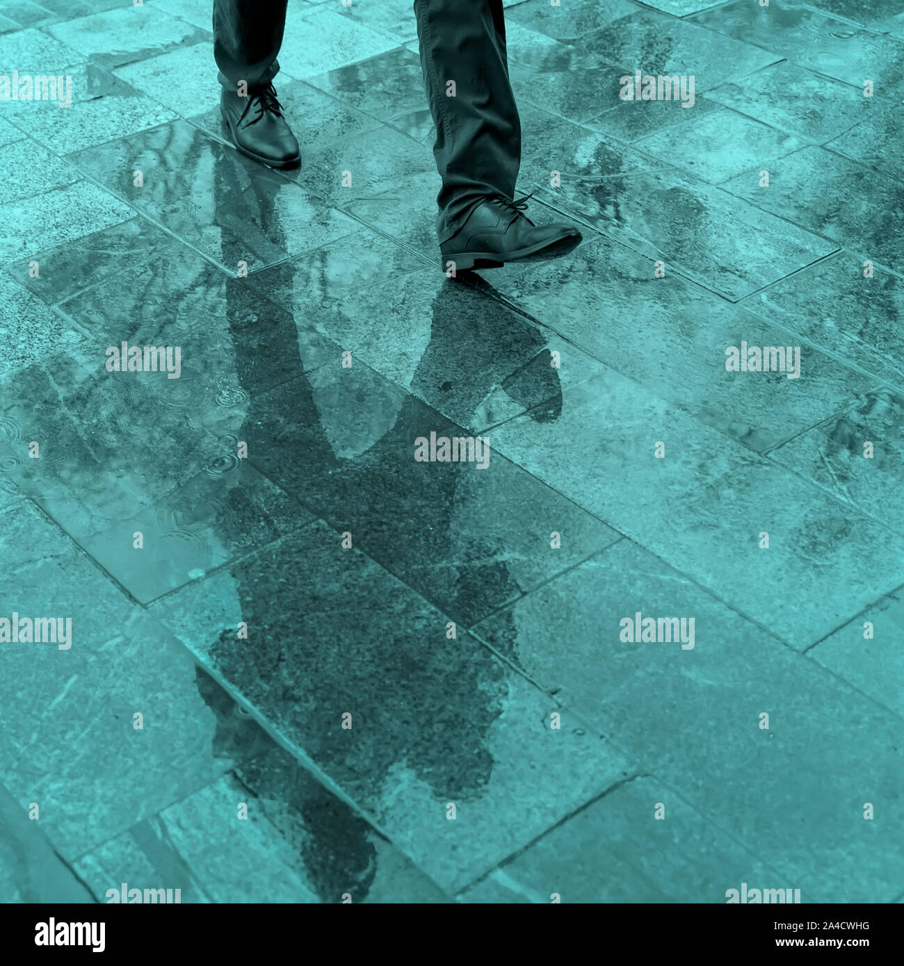 Sfocate gambe di riflessione e di ombra, silhouette di un uomo in un marciapiede in umido in una pozza camminando su un sensore pioggia Foto Stock