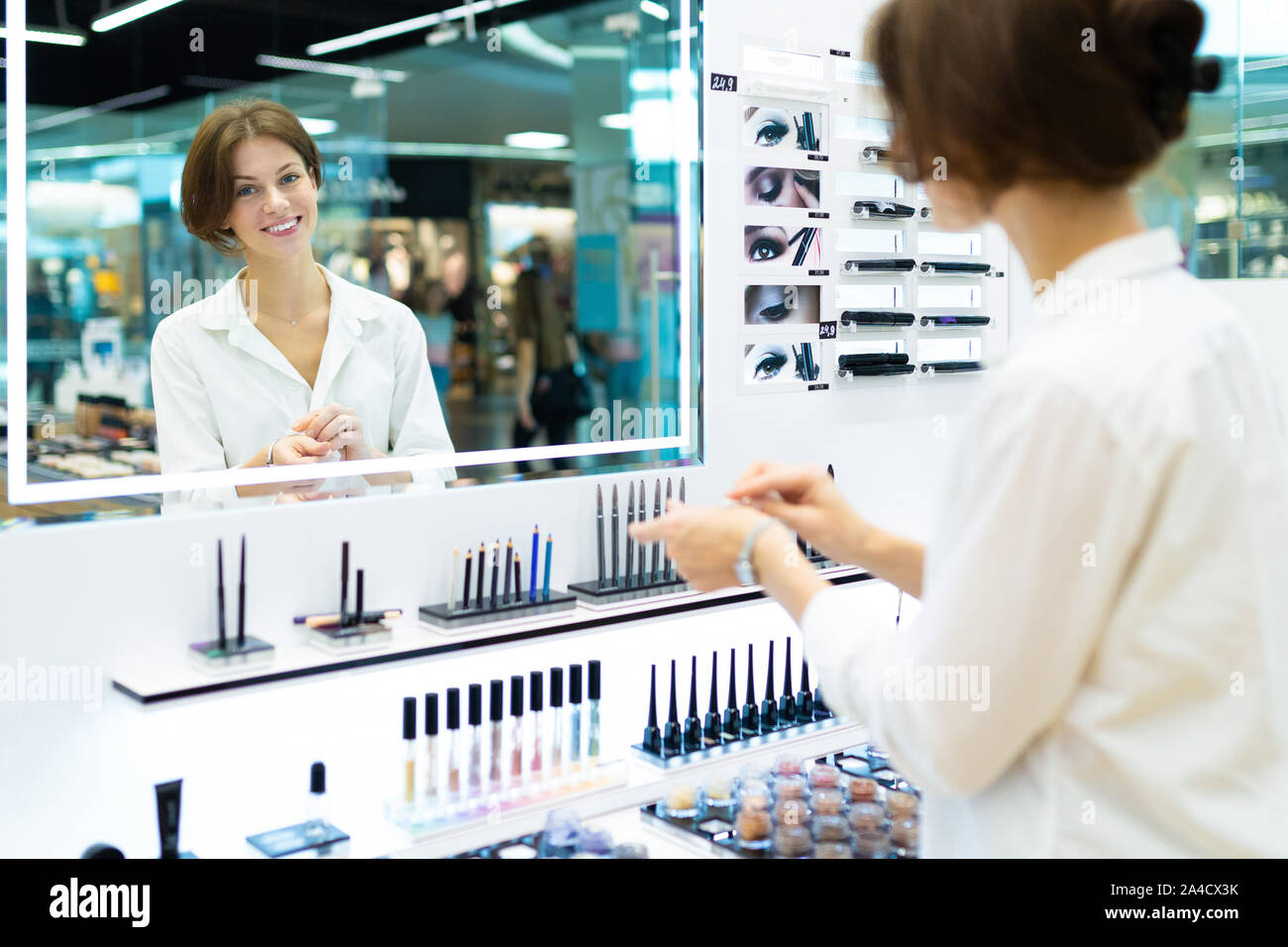 Giovane donna sorridente in un negozio di cosmetici è testare i cosmetici nella parte anteriore dello specchio Foto Stock