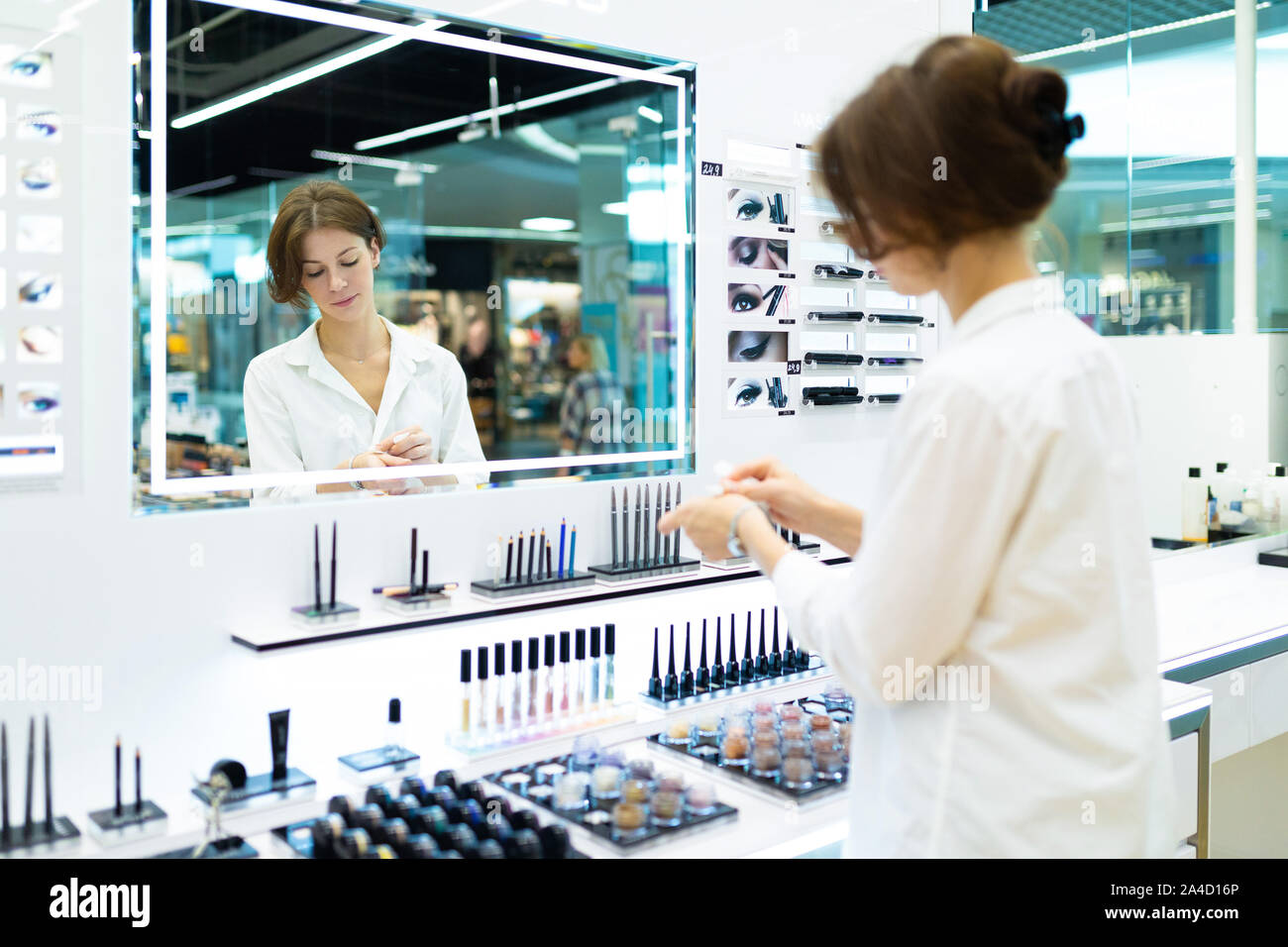 Giovane donna in un negozio di cosmetici è testare i cosmetici nella parte anteriore dello specchio Foto Stock