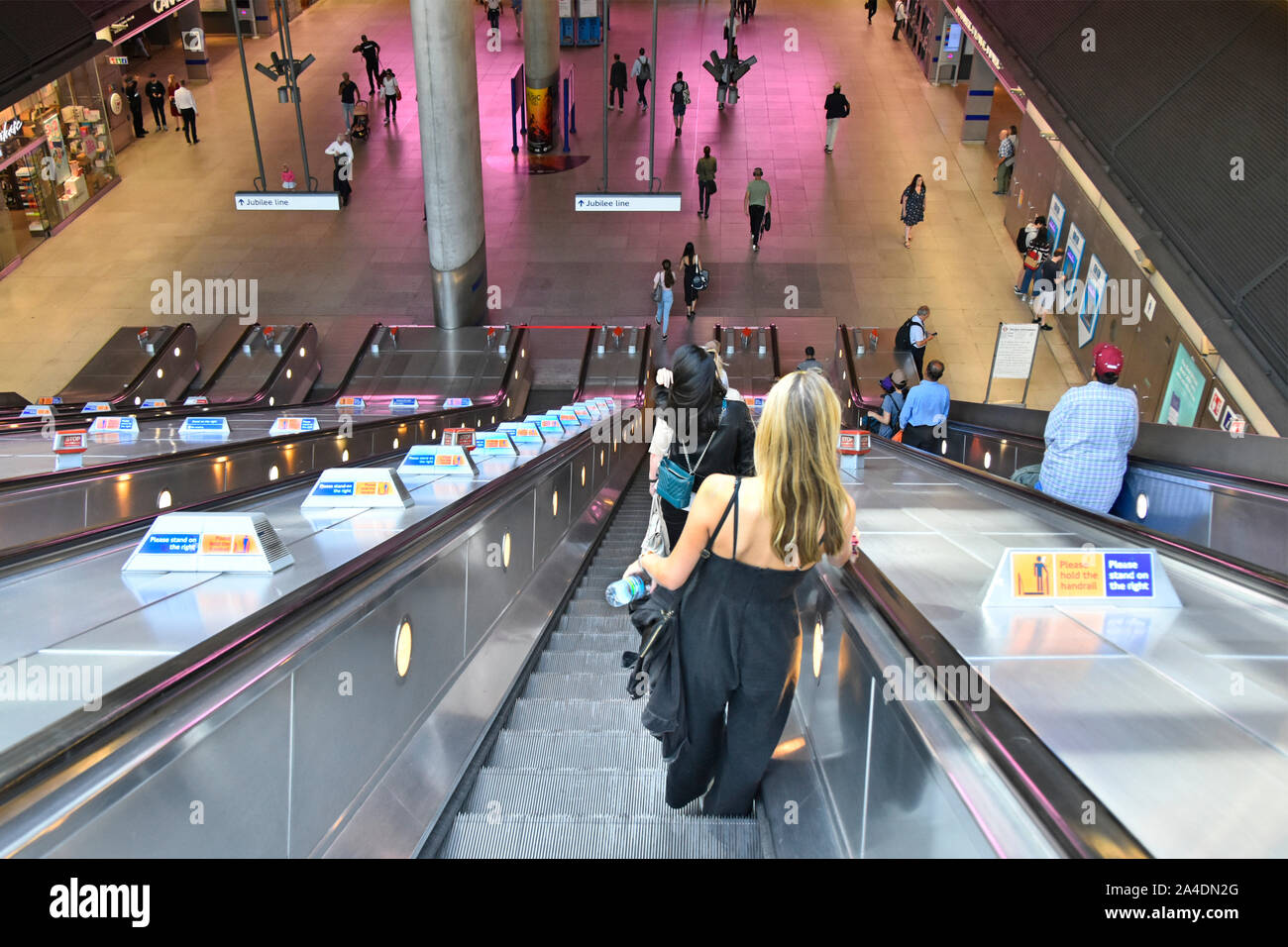 Giovane donna & altri passeggeri scendono sulla scala mobile al tubo della metropolitana treno servizi a Canary Wharf stazione ferroviaria Docklands di Londra Inghilterra REGNO UNITO Foto Stock