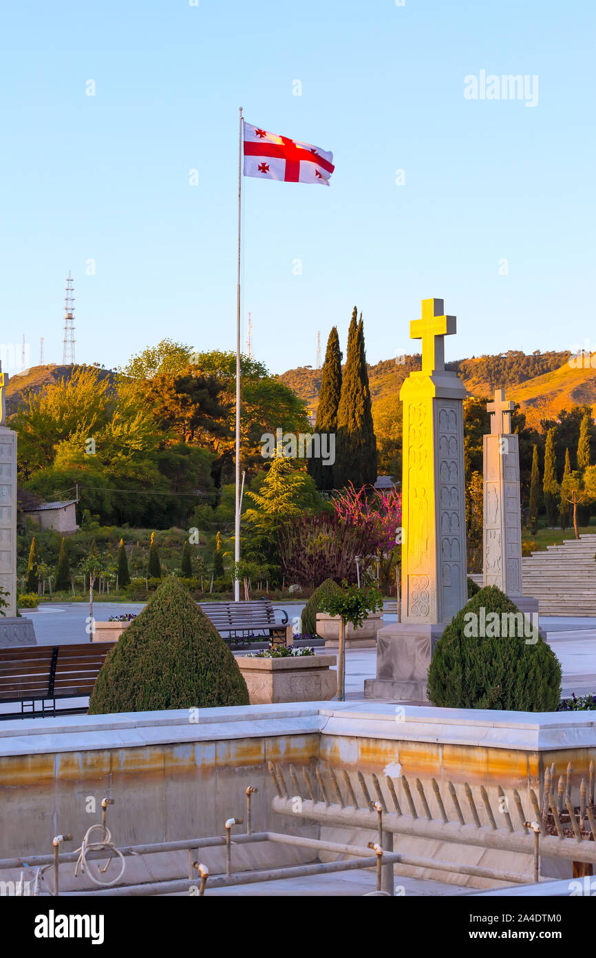Bandiera georgiana e croce vicino alla chiesa della Santa Trinità o Tsminda Sameba Cattedrale al tramonto a Tbilisi, Georgia Foto Stock