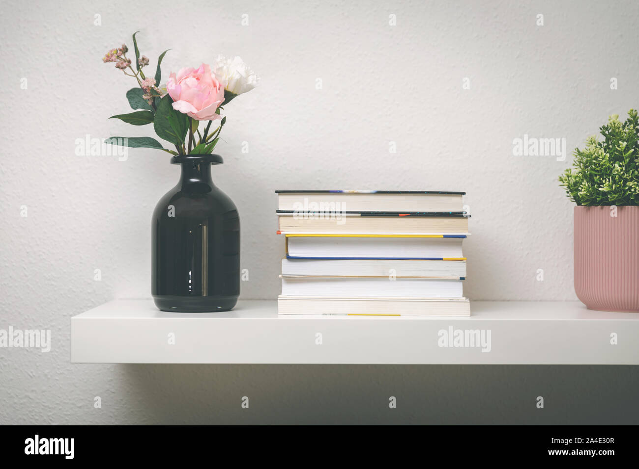 Ripiano sul muro bianco con libri e vasi di fiori Foto Stock