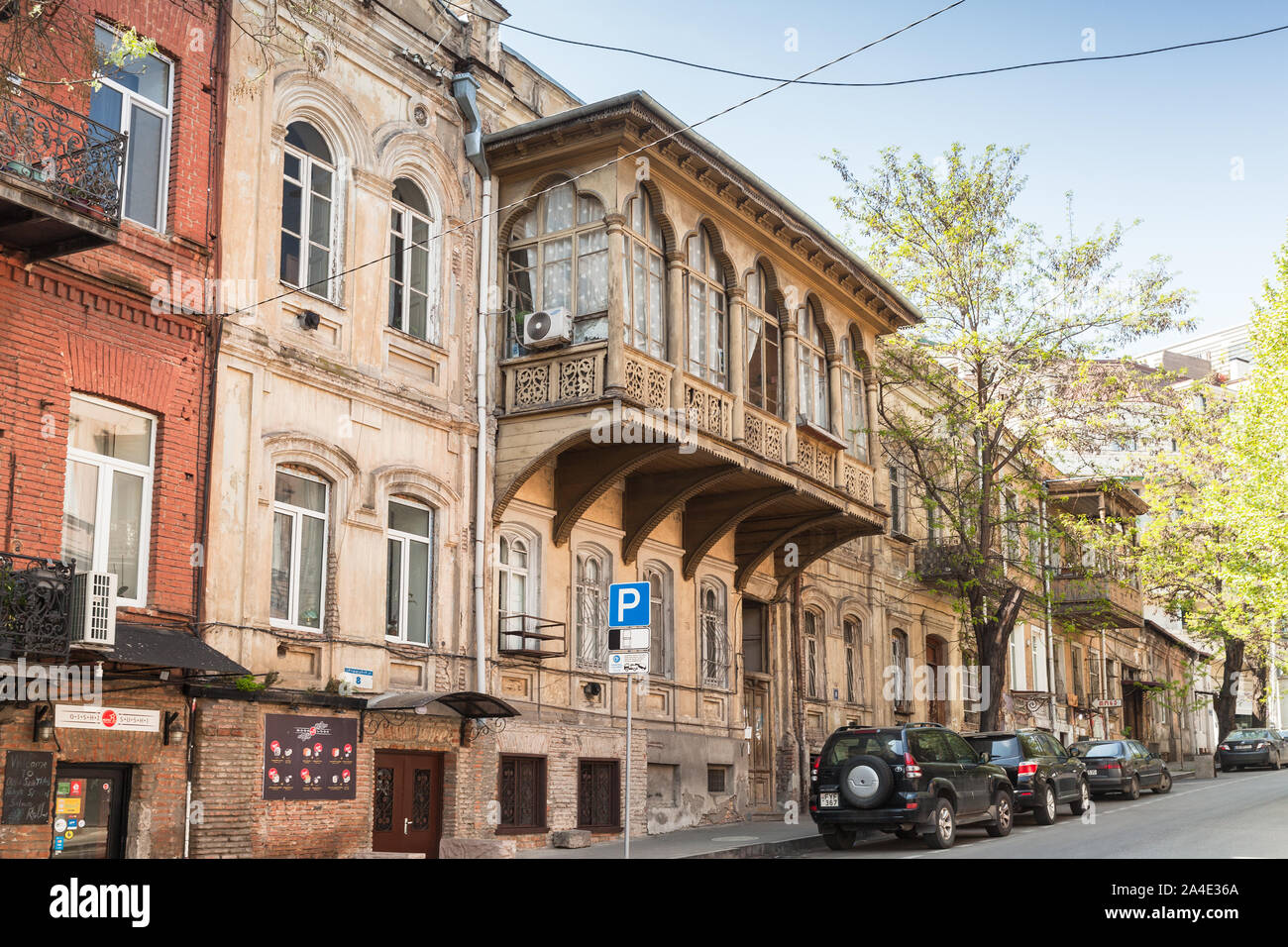 Tbilisi, Georgia - 28 Aprile 2019: Tbilisi street view con le auto parcheggiate vicino a vecchie case di vita tradizionale con balconi di legno scolpito Foto Stock
