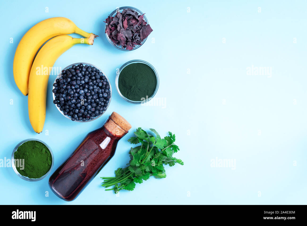 Heavy Metals Detox frullato. I mirtilli, mirtillo, orzo succo di erba estratto, spirulina polvere, succo di arancia, dulse e coriandolo su sfondo blu. Foto Stock