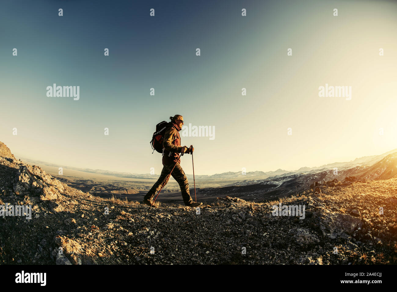 Escursionista cammina con zaino e bastoncini da trekking in montagna al tramonto Foto Stock