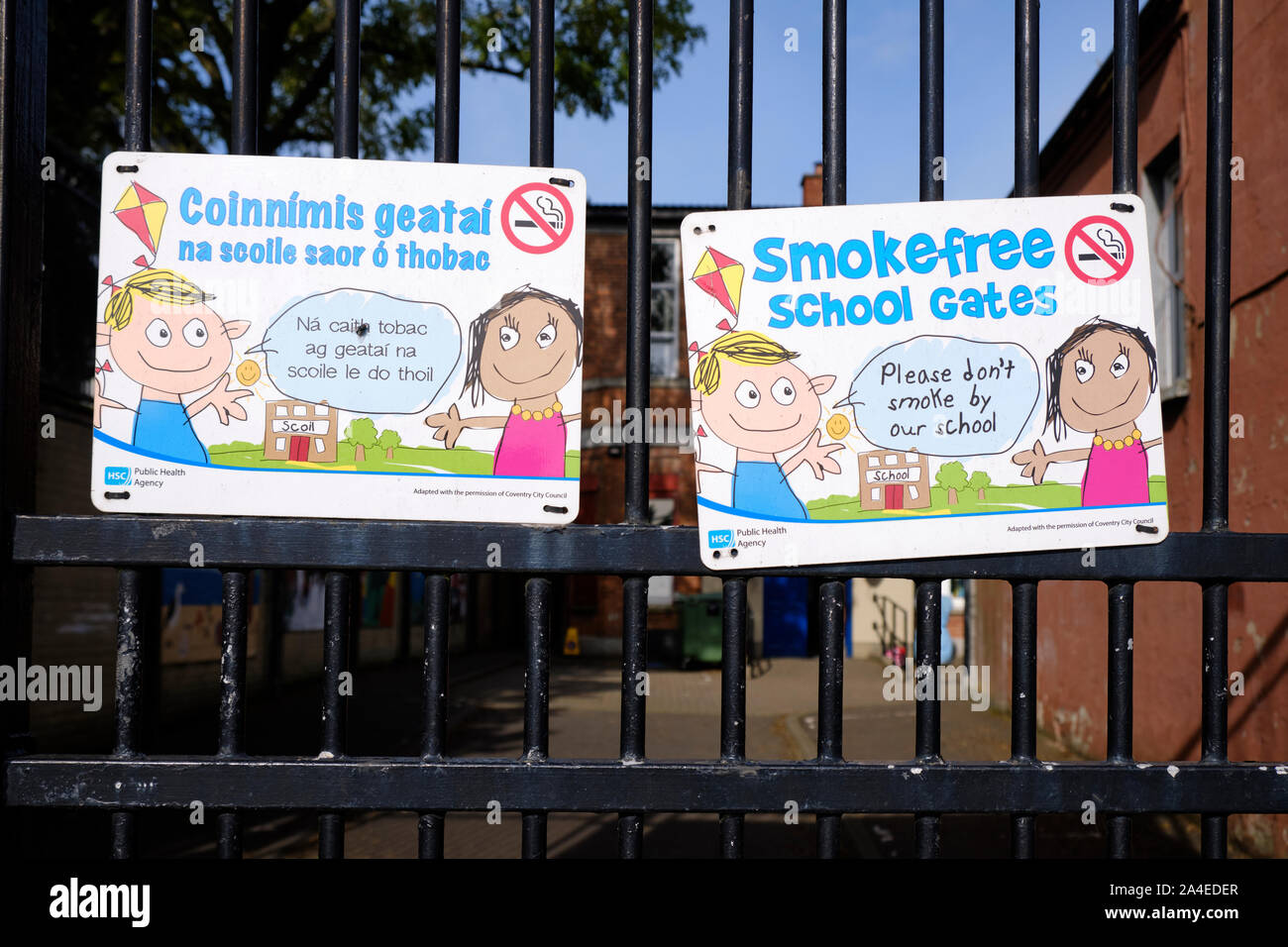 Segni bilingue inglese e lingua irlandese al di fuori di una Belfast West scuola, affermando senza fumo Scuole Foto Stock