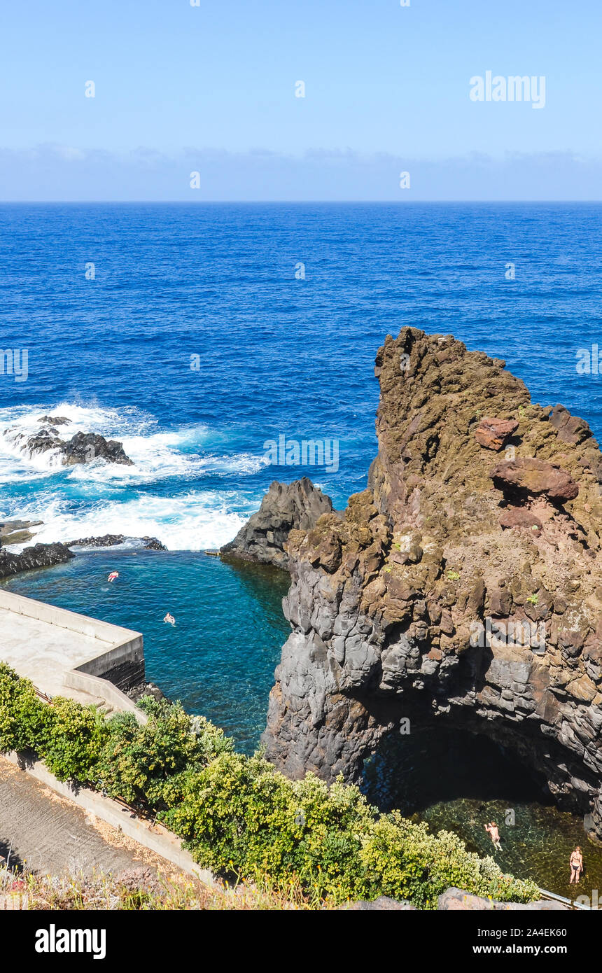 I turisti a nuotare in piscine naturali nell'oceano atlantico di Seixal, isola di Madeira, Portogallo. Piscina circondata da rocce di origine vulcanica dal mare aperto. Vista da sopra. La vacanza estiva di destinazione. Foto Stock