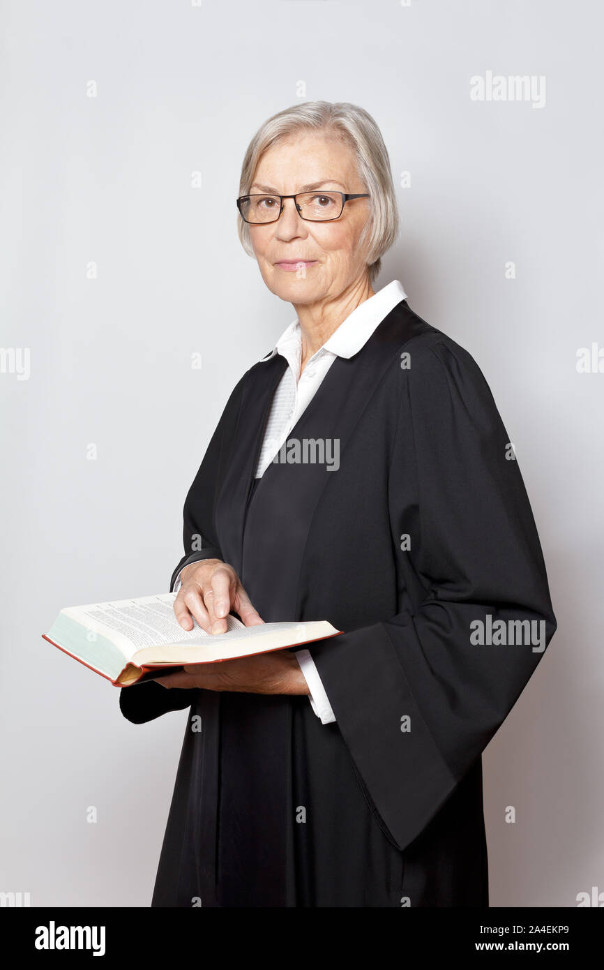 Avvocato femmina concetto: ritratto di una donna anziana in un abito nero tenendo un testo legislativo libro. Foto Stock