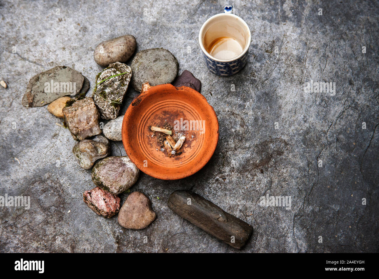 Posacenere con arrotolare sigarette sull'ardesia accanto a rocce e tazza da caffè Foto Stock