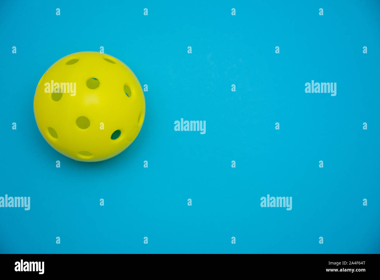 Di colore giallo brillante pickleball o sfera whiffle su un solido blu luminoso appartamento sfondo laici che simboleggiano sport e attività con copia spazio. Foto Stock