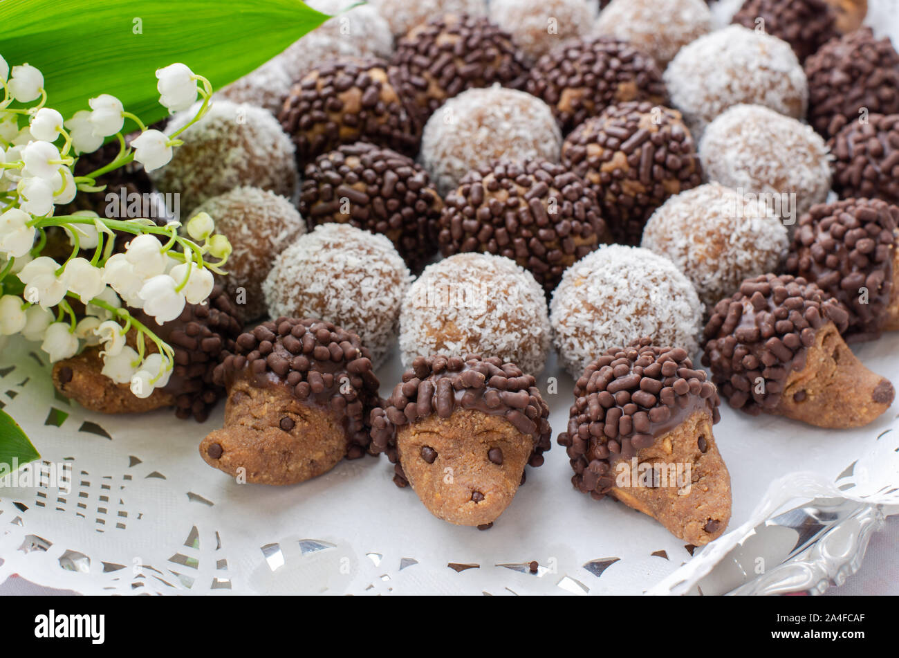 Piastra del Mini Riccio - cioccolato la pasticceria. Sulla piastra è anche il rum classici palle. La foto è decorato con fiori di colore bianco il giglio della valle. Foto Stock