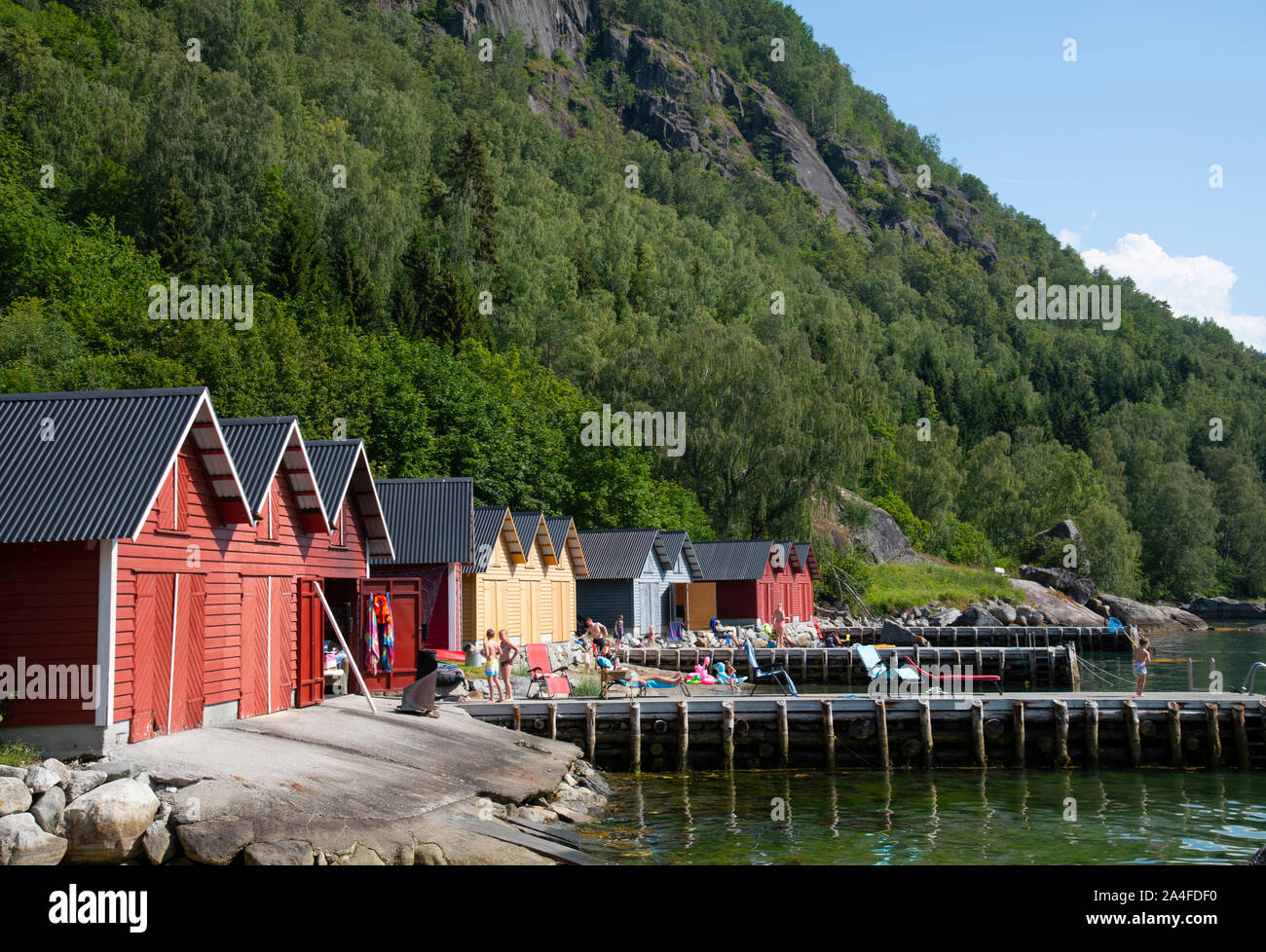 Sun bagnanti nella parte anteriore del legname di colorate case dock sul lungomare di Solvorn su Lustra fiordo, Vestlandet, Norvegia, Europa Foto Stock