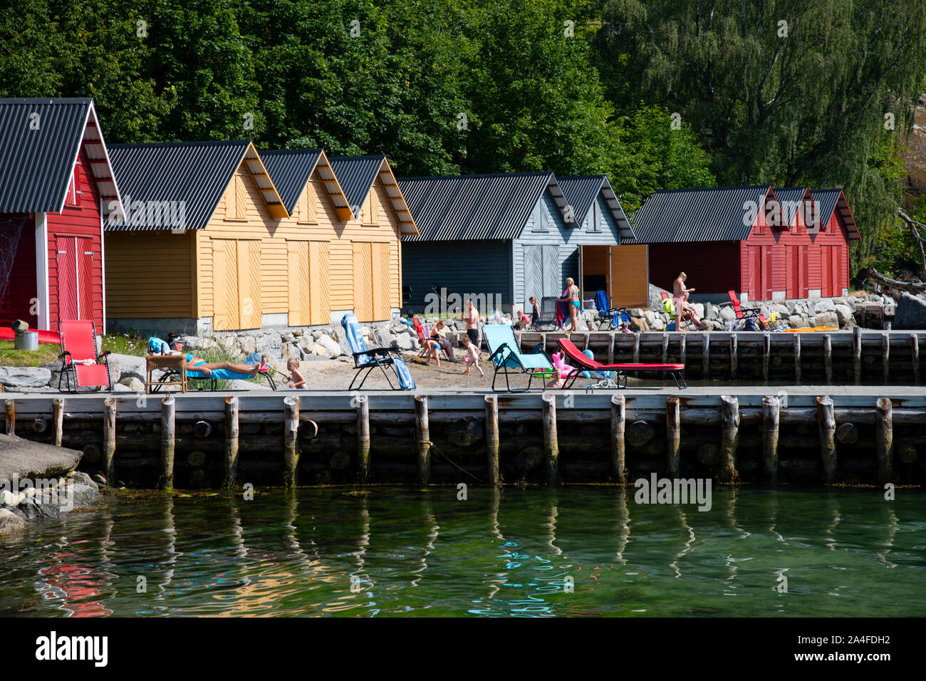 Sun bagnanti nella parte anteriore del legname di colorate case dock sul lungomare di Solvorn su Lustra fiordo, Vestlandet, Norvegia, Europa Foto Stock