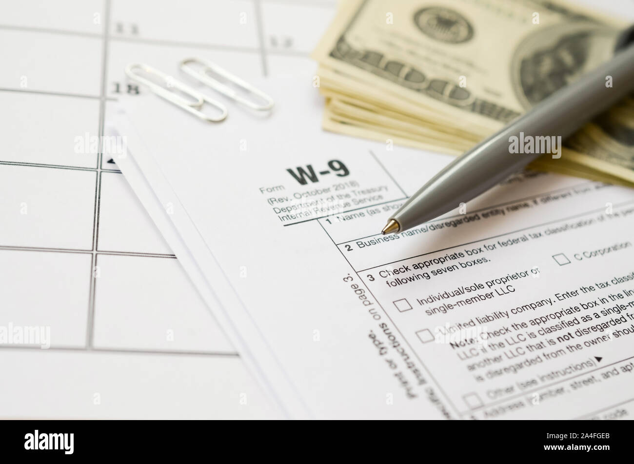 IRS Form W-9 richiesta per il contribuente un numero di identificazione e certificazione giace vuoto con penna e molte centinaia di fatture del dollaro nella pagina calendario. Imposta peri Foto Stock