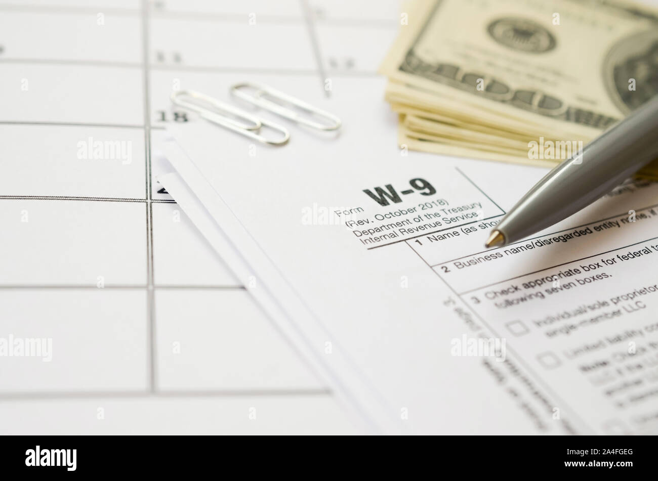 IRS Form W-9 richiesta per il contribuente un numero di identificazione e certificazione giace vuoto con penna e molte centinaia di fatture del dollaro nella pagina calendario. Imposta peri Foto Stock