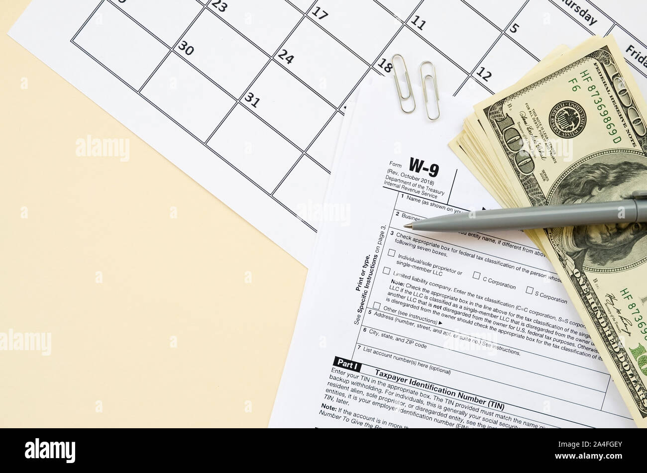 IRS Form W-9 richiesta per il contribuente un numero di identificazione e certificazione giace vuoto con penna e molte centinaia di fatture del dollaro nella pagina calendario. Imposta peri Foto Stock