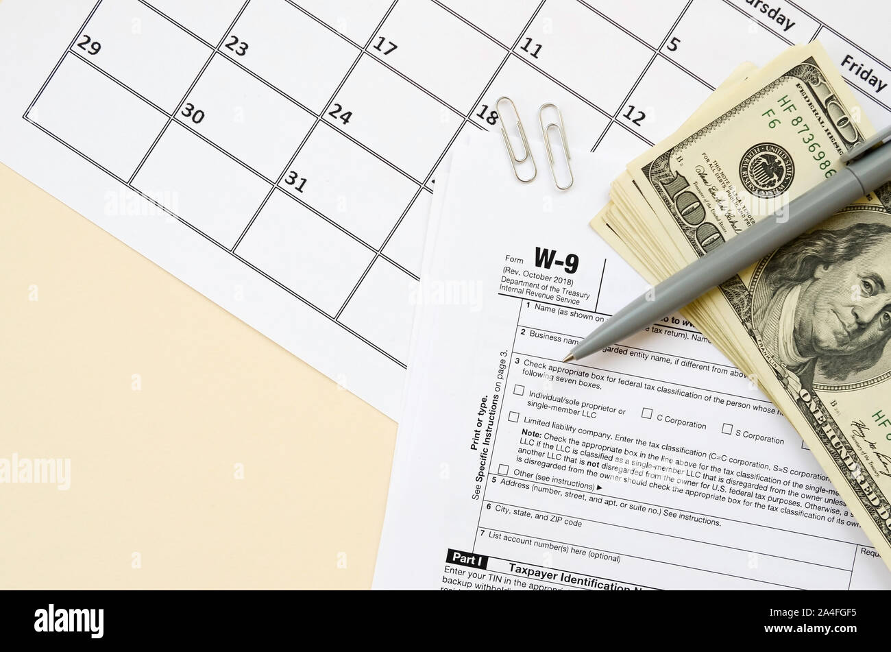 IRS Form W-9 richiesta per il contribuente un numero di identificazione e certificazione giace vuoto con penna e molte centinaia di fatture del dollaro nella pagina calendario. Imposta peri Foto Stock