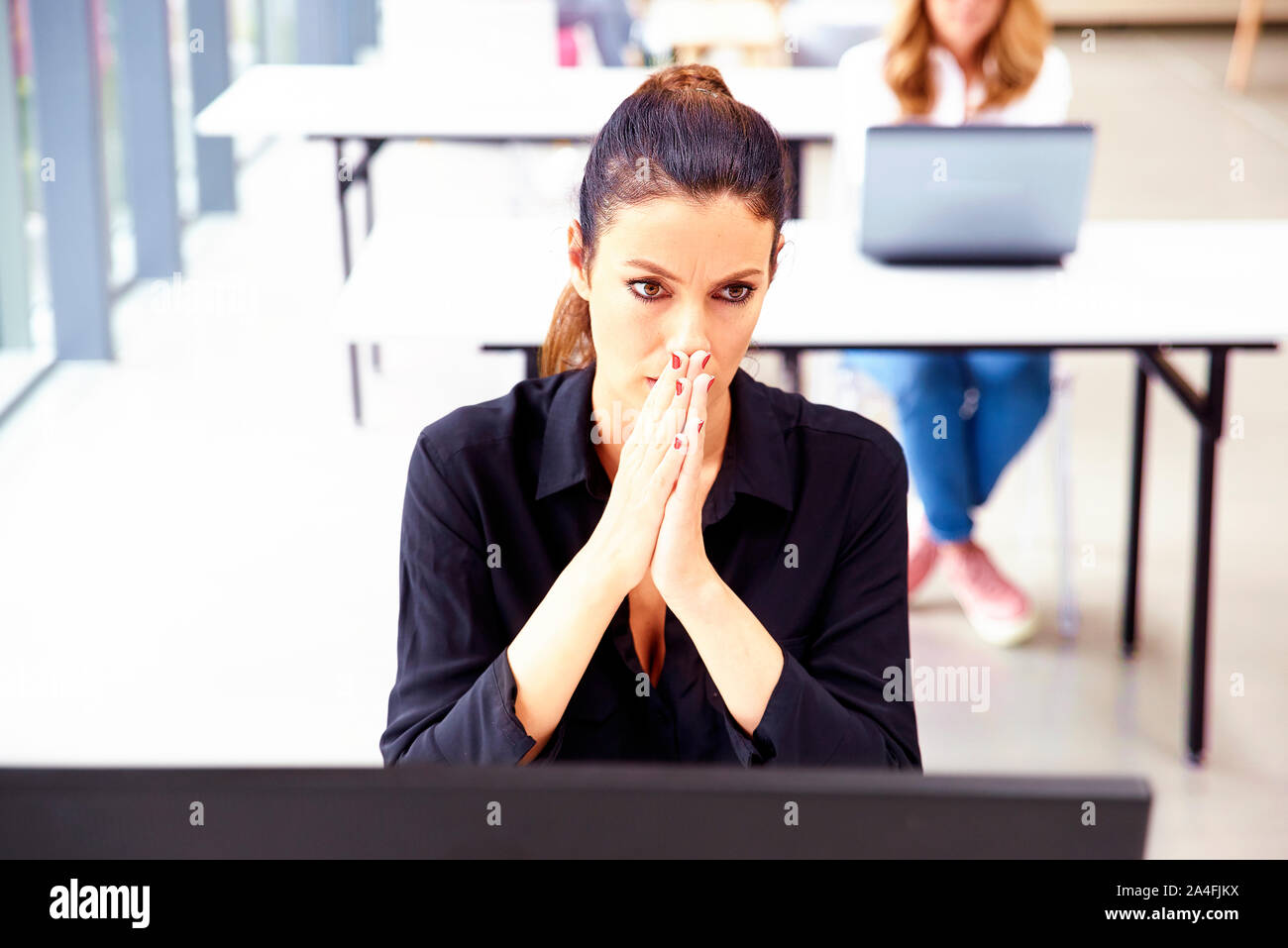 Imprenditrice con sconvolto l'espressione del viso seduto alla scrivania in ufficio dietro il suo computer. Foto Stock