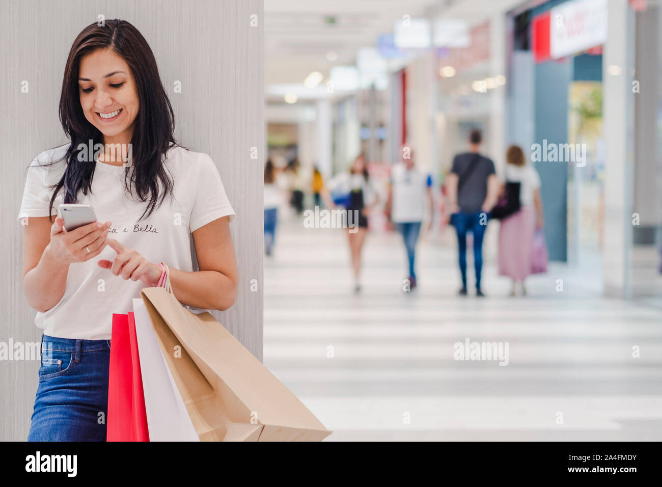 Venerdì nero, Donna utilizza lo smartphone e azienda shopping bag mentre si sta in piedi sul mall dello sfondo. L'immagine orizzontale. Foto Stock