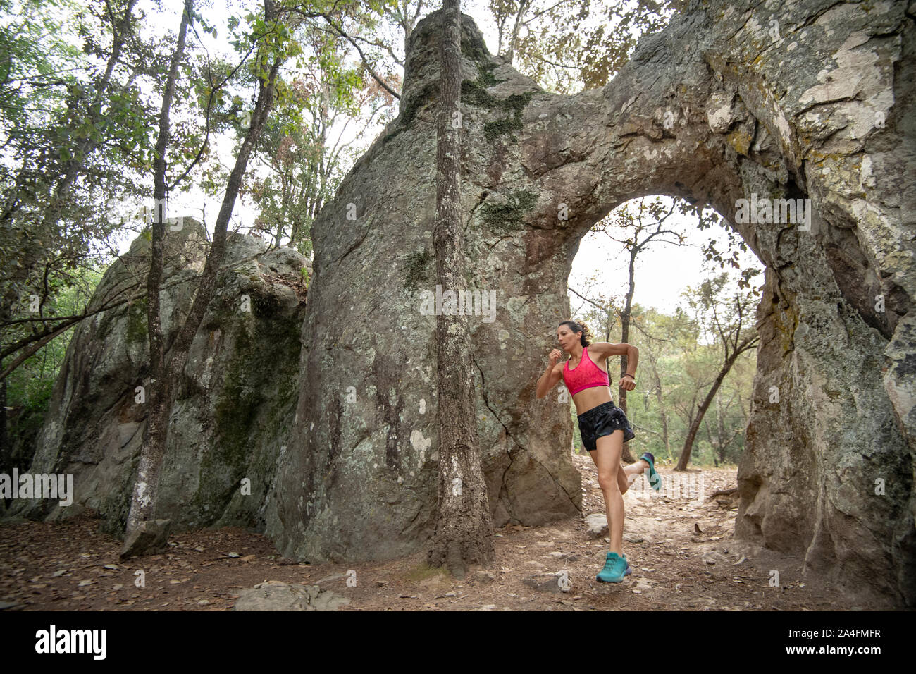Una donna nel suo 40s in esecuzione su shorts e un top rosa attraverso un arco naturale di roccia di El Arquito, Huasca de Ocampo, hidalgo, Messico. Foto Stock