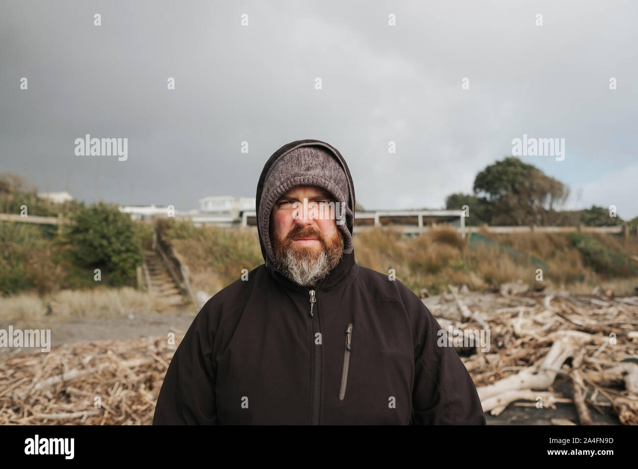 Uomo con barba permanente sulla spiaggia circondata da driftwood Foto Stock