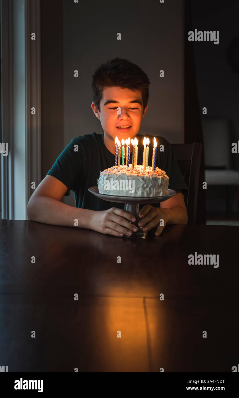 Teen boy guardando le candeline sulla sua torta di compleanno in una stanza buia. Foto Stock