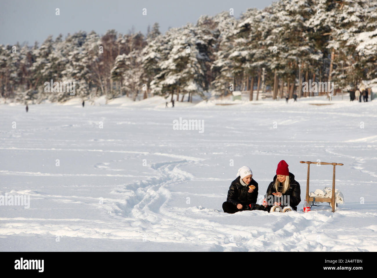 Due ragazze seduta con i loro telefoni cellulari e avente una giornata soleggiata sul lago Vättern's ice.Photo Jeppe Gustafsson Foto Stock