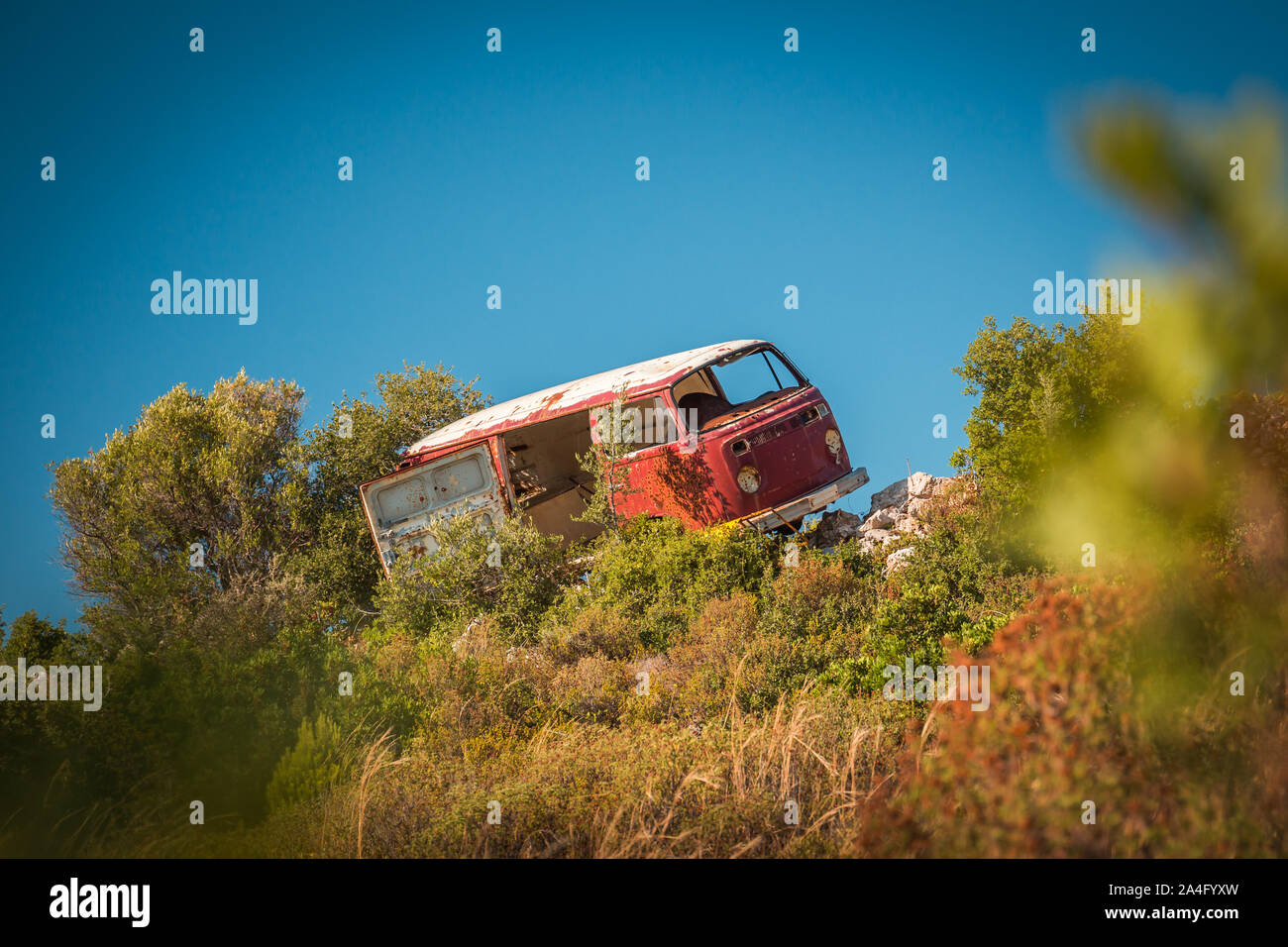 Abbandonato van bus su rocce nel mezzo del nulla in una giornata di sole. Al di fuori della messa a fuoco di alberi in primo piano, girato da distace. Foto Stock