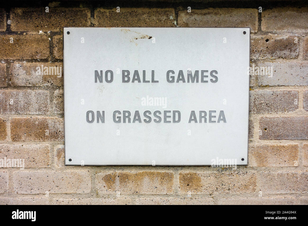 Un segno su un muro di mattoni di istruire la gente a non giocare a giochi con la palla su un adiacente prato, Foto Stock