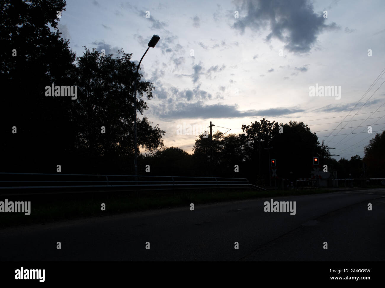 Vista su un treno in un attraversamento ferroviario con la persona in attesa sotto un cielo al distretto di Emsland nel nord ovest della Germania Foto Stock