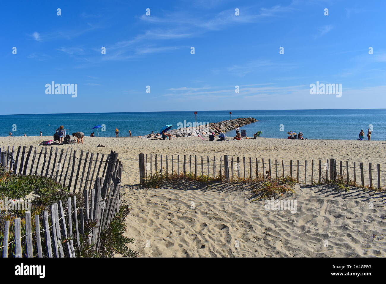 I vacanzieri godere il sole su di una spiaggia di sabbia nel sud della Francia. Niente bagnino. Mare calmo e pier in background. Foto Stock